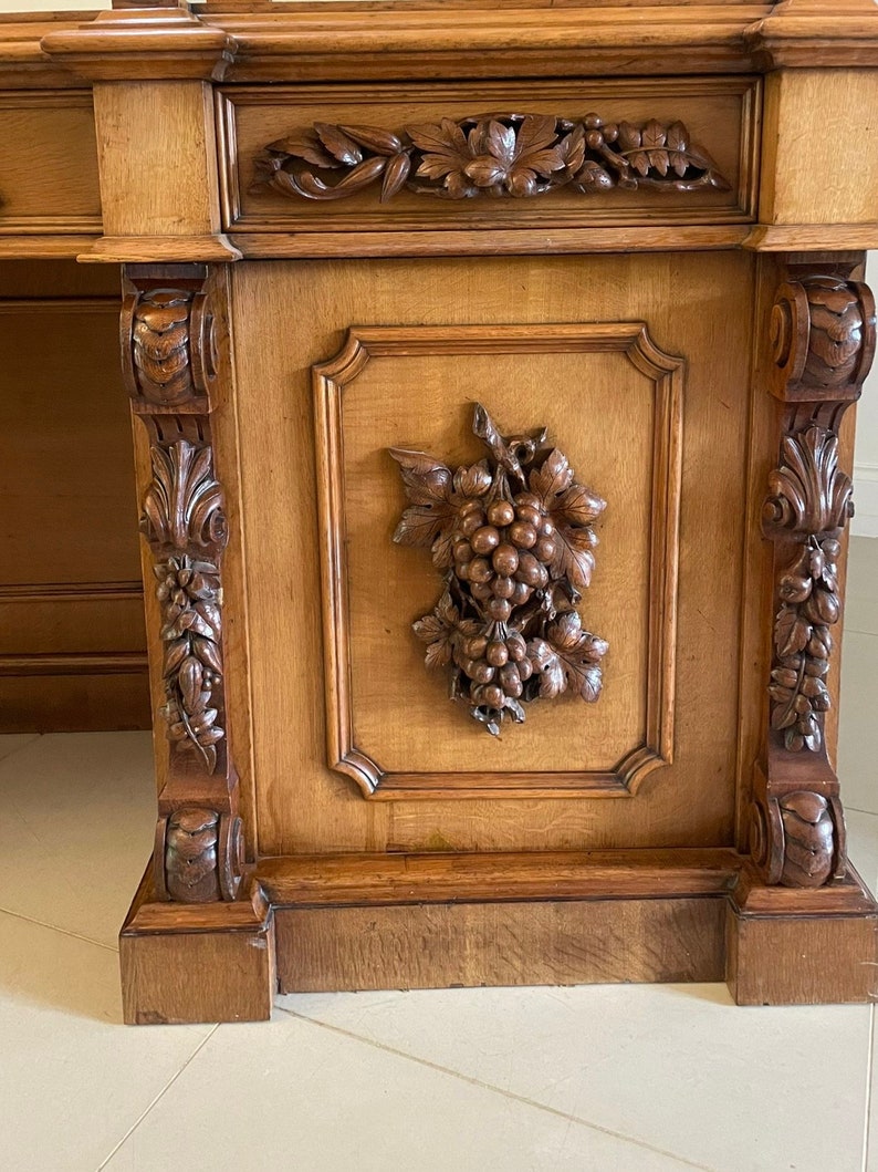 May include: A large, antique wooden cabinet with intricate carvings of grapes and leaves. The cabinet has a dark brown finish and is decorated with ornate details.