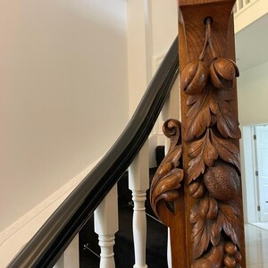May include: A close-up of a wooden staircase handrail with intricate carvings of leaves and fruit. The handrail is made of dark wood and has a black painted finish. The carvings are detailed and realistic, and the handrail is a beautiful example of craftsmanship.