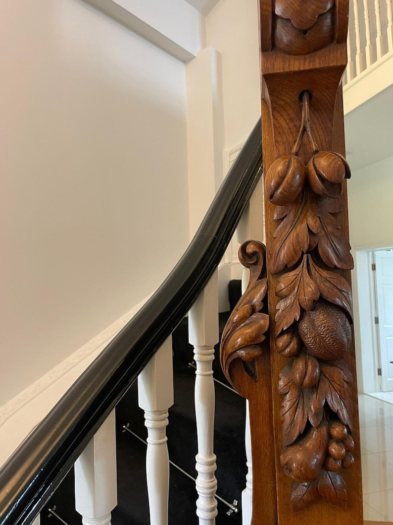 May include: A close-up of a wooden staircase handrail with intricate carvings of leaves and fruit. The handrail is made of dark wood and has a black painted finish. The carvings are detailed and realistic, and the handrail is a beautiful example of craftsmanship.