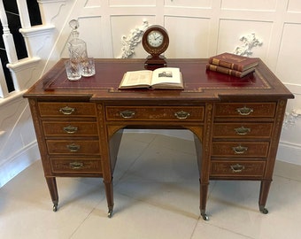 May include: A vintage wooden desk with a red leather top, featuring multiple drawers and ornate detailing. A clock, books, and glassware are arranged on the desk. The desk has a classic design with brass hardware and is set on a tiled floor.