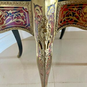 Puede incluir: Primer plano de una pata de mesa con intrincados detalles de marqueter&iacute;a dorada y roja. La pata est&aacute; tallada con un dise&ntilde;o decorativo y presenta una peque&ntilde;a cara adornada.