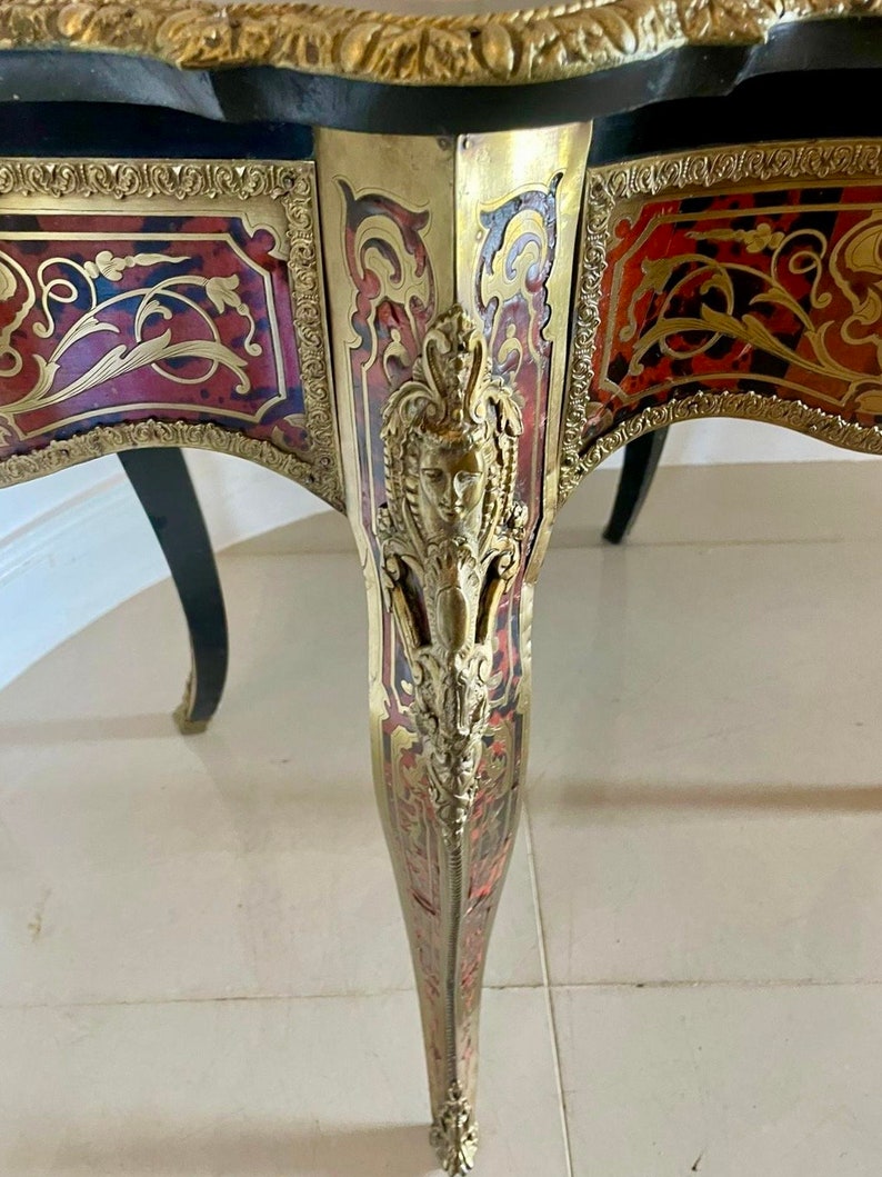 Puede incluir: Primer plano de una pata de mesa con intrincados detalles de marqueter&iacute;a dorada y roja. La pata est&aacute; tallada con un dise&ntilde;o decorativo y presenta una peque&ntilde;a cara adornada.
