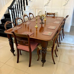May include: A mahogany dining table with eight chairs, set in a well-lit room. The table has a polished surface and stands on turned legs. The chairs feature patterned upholstery and curved backs. Gold candlesticks and a decorative bowl are on the table.