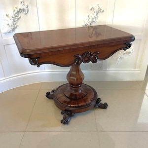 May include: A dark wood, antique style,  game table with a carved base and ornate legs. The table has a rectangular top and a single pedestal base.