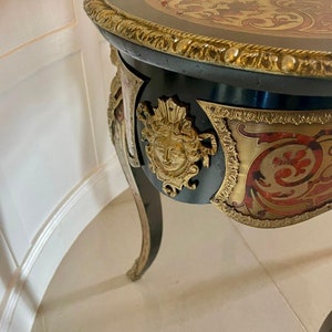 Puede incluir: Una mesa ornamentada negra y dorada con una tapa de marqueter&iacute;a y un dise&ntilde;o tallado. La mesa tiene tres patas y un borde decorativo alrededor de la parte superior.
