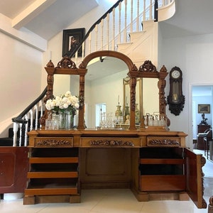 May include: A large, ornately carved wooden cabinet with three mirrored doors and multiple drawers. The cabinet has a rich brown finish and intricate details.