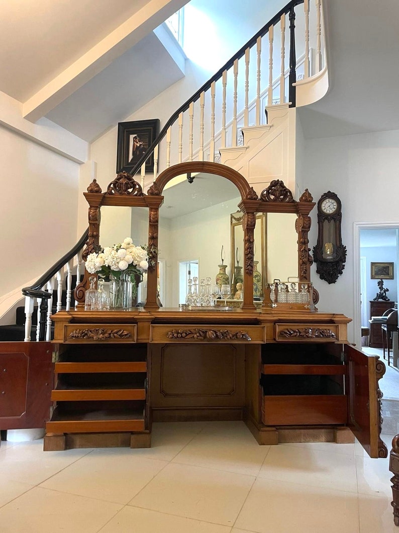 May include: A large, ornately carved wooden cabinet with three mirrored doors and multiple drawers. The cabinet has a rich brown finish and intricate details.
