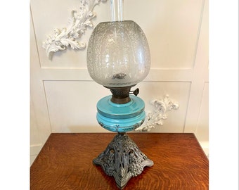 May include: A vintage oil lamp with a frosted glass shade and a turquoise blue base. The lamp has a decorative metal base with intricate details.