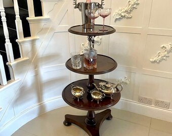 May include: A three-tiered mahogany serving stand with a round top, featuring a silver ice bucket with a bottle of champagne and two pink stemmed glasses on the top tier. The middle tier has a decanter and a glass, and the bottom tier has a silver teapot and two silver sugar bowls.