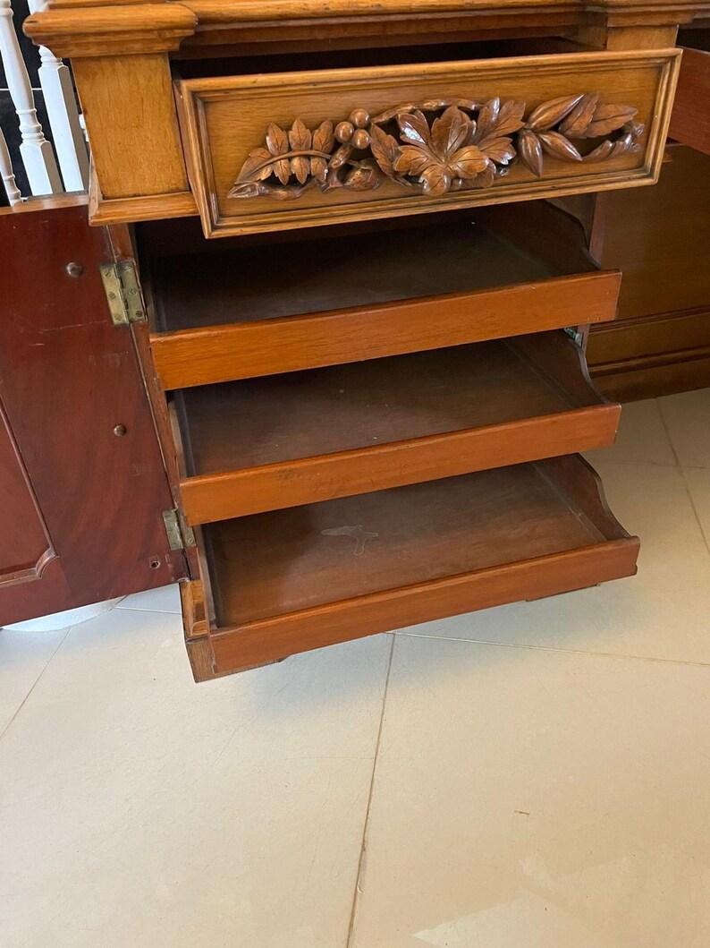 May include: A wooden cabinet with a carved drawer and four open shelves. The cabinet is made of light wood and has a dark wood finish. The shelves are empty.