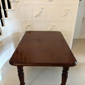 Puede incluir: Una mesa de madera de color marrón oscuro con tapa rectangular y patas torneadas. La mesa tiene un acabado liso y pulido y está sobre ruedas.