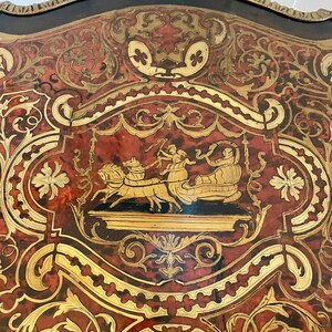Puede incluir: Un primer plano de una mesa con un intrincado trabajo de marqueter&iacute;a. El dise&ntilde;o presenta un carro tirado por caballos y figuras en oro y rojo sobre un fondo negro.