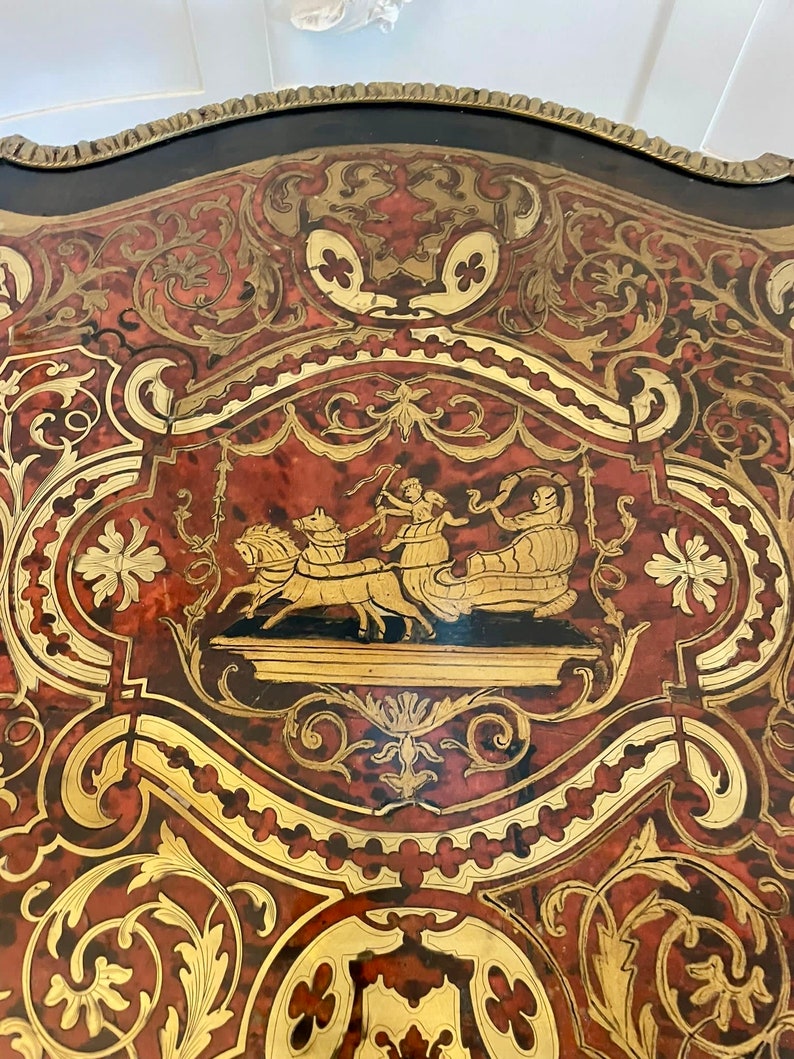 Puede incluir: Un primer plano de una mesa con un intrincado trabajo de marqueter&iacute;a. El dise&ntilde;o presenta un carro tirado por caballos y figuras en oro y rojo sobre un fondo negro.