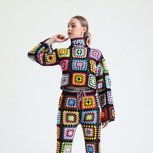 May include: A crochet top and trousers set in black with colourful square patterns. The top has a mock neck and long sleeves. The trousers are flared and have a drawstring waist.