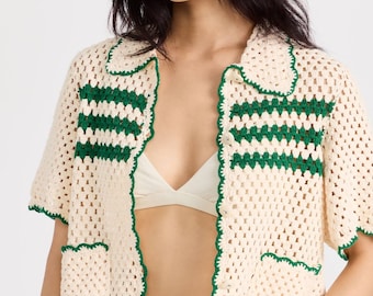 May include: A white crochet cardigan with green trim. The cardigan has a collar and short sleeves.