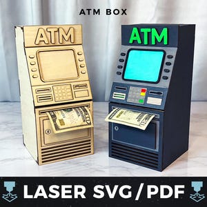 Op de afbeelding: Twee decoratieve ATM-dozen, één in natuurlijk hout en de andere in donkergrijs, elk met het woord "ATM" erboven. Een twintig dollar biljet is gedeeltelijk zichtbaar in de geldautomaat van elke doos. De tekst "ATM BOX" en "LASER SVG/PDF" zijn ook zichtbaar.
