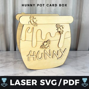 May include: A wooden card box shaped like a honey pot, with the word "HUNNY" cut out on the front. The design includes dripping honey and bee cutouts. The text "HUNNY POT CARD BOX" is at the top. The bottom text reads "LASER SVG/PDF".