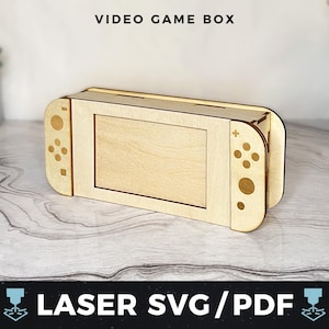 May include: A light-coloured wooden video game box, designed to look like a games console. It has a screen and controller details. The text "VIDEO GAME BOX" is at the top, and "LASER SVG/PDF" is at the bottom.