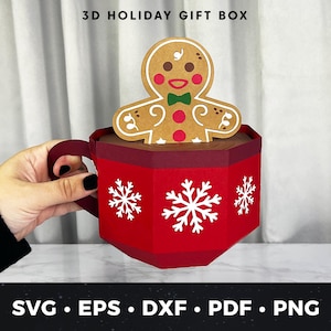 May include: A red 3D holiday gift box shaped like a mug, with white snowflake cutouts. A gingerbread man cutout sits inside the mug. The mug has a handle and is held by a person. Text on the image reads "3D HOLIDAY GIFT BOX" and "SVG • EPS • DXF • PDF • PNG".