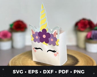 May include: A white unicorn-themed favor box with a yellow horn, purple flowers, and pink hearts. The box is perfect for holding small gifts or treats.