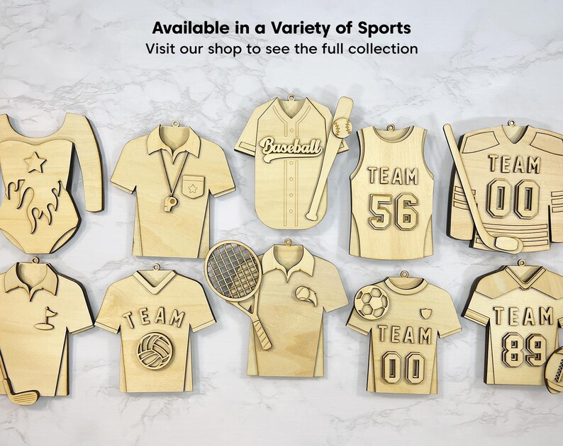 May include: A collection of wooden sports-themed decorations, featuring a gymnastics leotard, baseball jersey, and hockey jersey. The text reads "Available in a Variety of Sports" and "Visit our shop to see the full collection".
