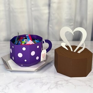 May include: A purple teacup with white polka dots filled with colorful candy. The teacup has a handle and a pink heart tag. A brown box with a white heart shaped steam design sits next to the teacup.