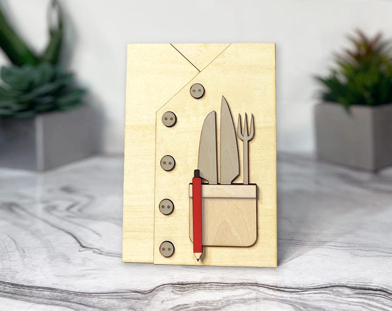 May include: A wooden cutout of a chef's jacket with a pocket containing a knife, fork, and pencil. The jacket has four buttons.