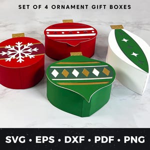 Könnte beinhalten: Set aus vier ornamentförmigen Geschenkboxen in Rot, Grün und Weiß. Die roten Boxen haben weiße Schneeflocken- und Streifendesigns. Die grüne Box hat ein Rautenmuster. Goldene Akzente und der Text "SET OF 4 ORNAMENT GIFT BOXES" sind sichtbar.