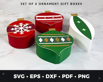 May include: Set of four ornament-shaped gift boxes in red, green, and white. The red boxes feature white snowflake and stripe designs. The green box has a diamond pattern. The white box has a green leaf design. Gold accents and the text "SET OF 4 ORNAMENT GIFT BOXES" are visible.