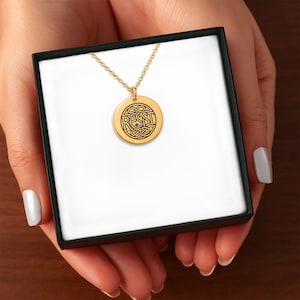 Puede incluir: Collar con colgante dorado con un dije redondo. El dije presenta el nombre "ROSSI" en letras negras, rodeado por un intrincado diseño de nudo celta. El collar se presenta en una caja de regalo negra con interior blanco.