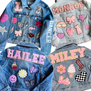 Puede incluir: Cuatro chaquetas vaqueras con diferentes parches y nombres en la espalda. Los nombres son Hailey, Miley, Monroe y L. Los parches incluyen un arcoíris, una magdalena, una mariposa, un corazón, una estrella, una flor, una bota vaquera, un cono de helado, un lazo, una zapatilla de bailarina, un pintalabios, un rayo, un diamante, una cara sonriente, un logotipo de Barbie, un patrón de cuadros y un oso.