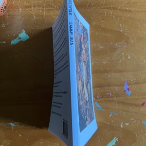 May include: A blue book with the title "LIFECYCLE" and the author's name "SAMMY JEAN" printed on the spine. The cover features a photograph of a woodland scene with a person standing in the middle.