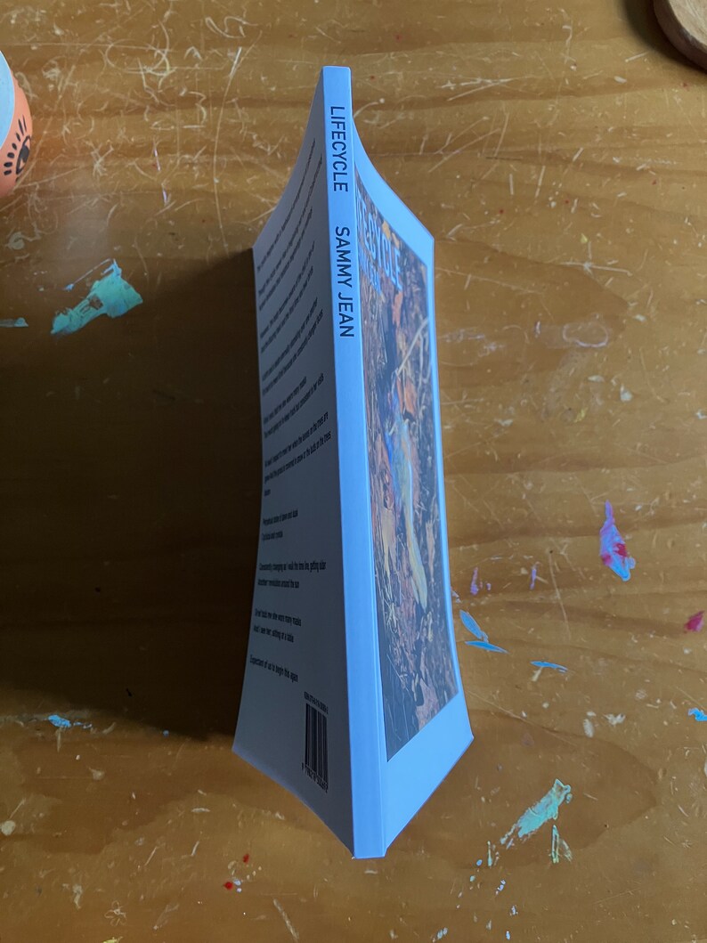 May include: A blue book with the title "LIFECYCLE" and the author's name "SAMMY JEAN" printed on the spine. The cover features a photograph of a woodland scene with a person standing in the middle.