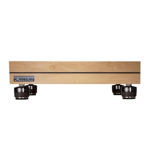 May include: A rectangular light-colored wooden platform featuring a horizontal black stripe and a blue and white label that reads Butcher Block Acoustics. The platform is supported by four black cylindrical feet with metallic accents.