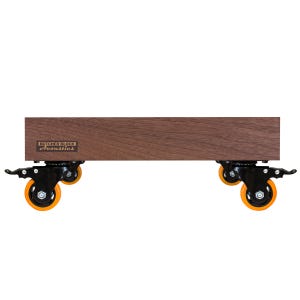 May include: A rectangular dark brown wooden platform featuring a Butcher Block Acoustics logo on the side. The platform is supported by four black metal swivel casters, each equipped with bright orange wheels and a locking lever mechanism.