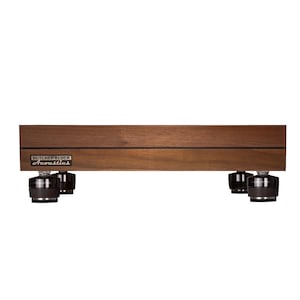 May include: A rectangular dark brown wooden audio isolation platform with a horizontal black inlay line. The front left corner features a metal badge with the text Butcher Block Acoustics. Four black cylindrical isolation feet support the base.
