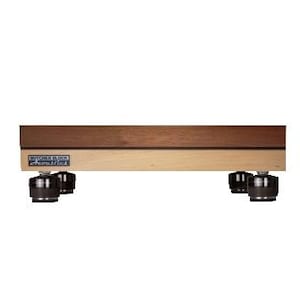 May include: A rectangular wooden platform featuring a dark brown top layer and a lighter tan bottom layer. The front edge displays a blue and white label reading Butcher Block Acoustics. Four black cylindrical feet are attached to the underside.
