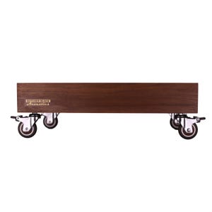 May include: A rectangular dark brown wooden platform featuring a smooth grain finish and four silver metal swivel casters with locking mechanisms. A gold-colored rectangular plaque on the front displays the text Butcher Block Acoustics.