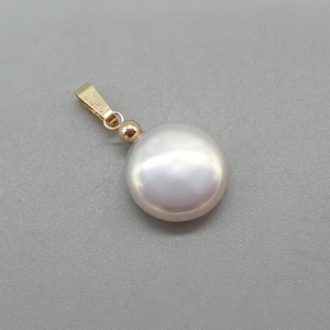 May include: A gold pendant with a large, white, round pearl. The pearl has a smooth, reflective surface. The pendant has a simple gold bail and a small gold bead. The background is a plain grey. The pearl is a classic jewellery piece.