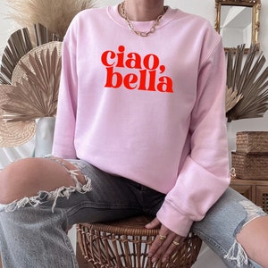 May include: A pink sweatshirt with the text "ciao, bella" in red letters.