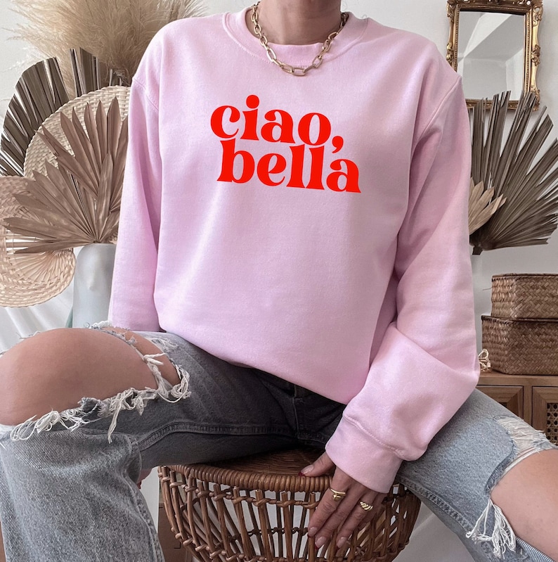 May include: A pink sweatshirt with the text "ciao, bella" in red letters.