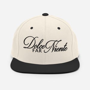 May include: A beige and black baseball cap with the text "Dolce Far Niente" embroidered in black cursive script.