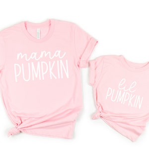 May include: Two pink t-shirts with white text. The larger shirt says "mama pumpkin" and the smaller shirt says "lil pumpkin".