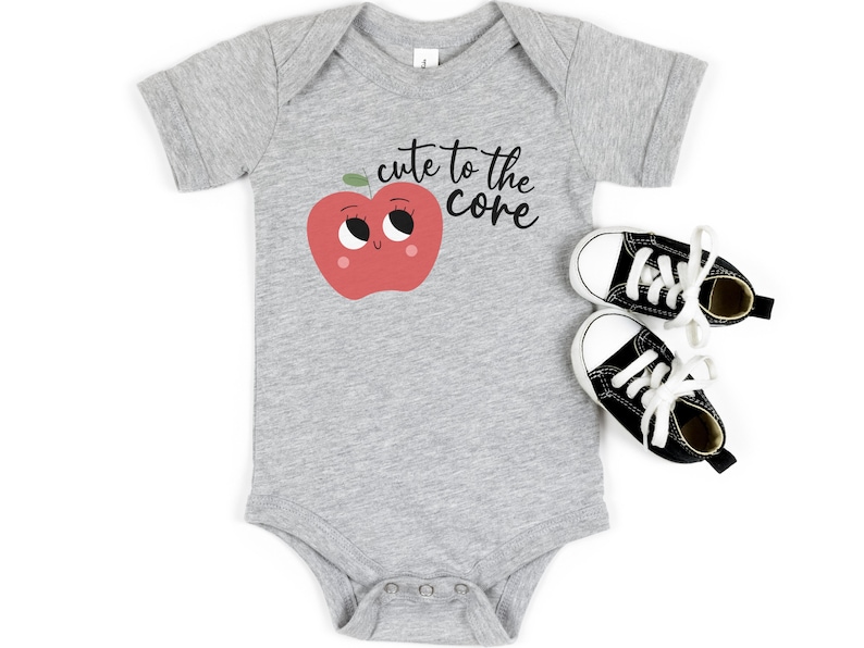K&ouml;nnte beinhalten: Ein grauer Baby-Strampler mit einem roten Apfel-Motiv und dem Text "cute to the core".