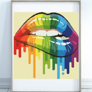 May include: A framed cross-stitch art piece featuring a pair of lips in a vibrant rainbow gradient. The lips have a glossy finish and are dripping with colorful paint. The artwork is set against a light yellow background.