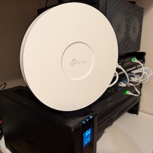 May include: A white TP-Link wireless router with a black power cord plugged into a black APC backup power supply with a digital display showing 1:31.
