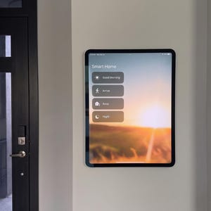May include: A tablet mounted on a wall displaying a Smart Home interface with buttons labeled Good Morning, Arrive, Away, and Night over a sunrise background. The screen shows a status bar at the top with the time and battery percentage.