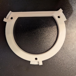 May include: White plastic ring with a raised edge and three small holes. The ring is designed to be attached to a surface.