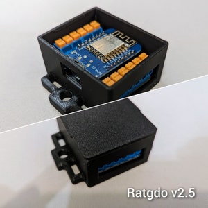 Pode incluir: Uma caixa de plástico preto com uma placa de circuito azul no seu interior. A placa tem um pequeno chip com o texto "Ratgdo v2.5" impresso nele.