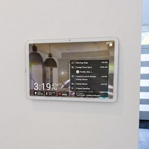 May include: A rectangular wall-mounted smart home display with a white frame. The screen shows a digital interface with the time 3:19 PM, a temperature of 58°F, a calendar list of daily tasks, and status icons for lights, thermostat, and security system.
